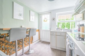 A kitchen with a bar area, a window with a view of greenery, and a door with a wreath. - Cosy 18th-Century Lake District Retreat with Charm & Comfort (Little Broughton)