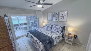 Ein Schlafzimmer mit einem Bett, einem Deckenventilator, einem Nachttisch und Blick auf eine Terrass.