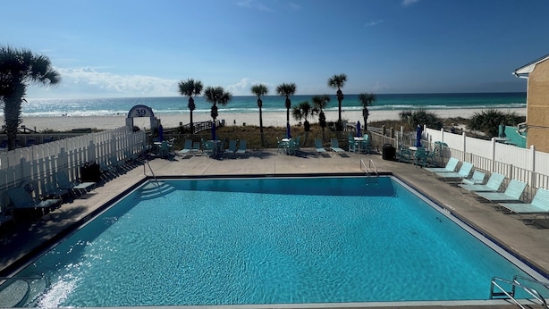 Ein Poolbereich mit Blick auf den Strand, Palmen und einen klaren Himmel.