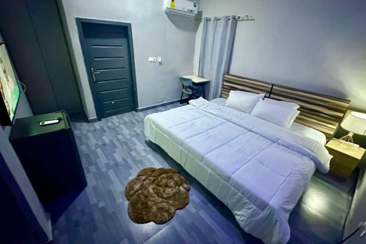 Une chambre d’hôtel avec un lit, une table de chevet, une lampe et un petit tapis rond.