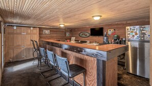 Una cocina con paneles de madera, una barra con taburetes, un refrigerador y un televisor montado en la pared.