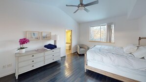 A bedroom with a bed, dresser, chair, ceiling fan, and a window.