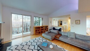A spacious living room with a large sofa, a coffee table, a bookshelf, and a sliding glass door leading to a balcony.