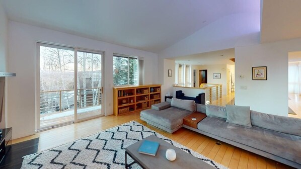 A spacious living room with a large sofa, a coffee table, a bookshelf, and a sliding glass door leading to a balcony.