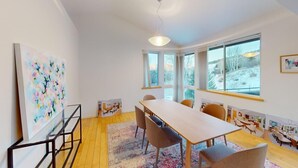 A modern interior with a long table, chairs, a large abstract painting, and a view of a snowy landscape through the windows.