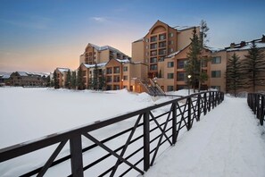 Ett snötäckt utomhusområde med ett trästaket, byggnader med flera våningar och balkonger samt snötäckta träd.