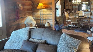 Ein rustikales Blockhaus-Interieur mit Ledersofa, Holzwänden, einem Essbereich und einer Kristallleuchter.
