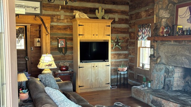 Ein Blockhaus-Interieur mit Holzbalkendecke, Kamin aus Stein, Ledersofa und Fernseher.