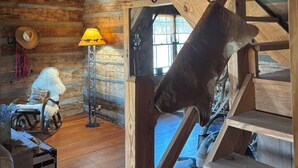 Ein rustikales Holzinnenleben mit einer Holztreppe, einer Lampe, einem Sessel mit Kissen und einem Fenster.