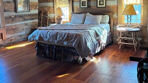 Ein rustikales Schlafzimmer in einer Blockhütte mit einem großen Bett, einem Deckenventilator und Holzwänden.