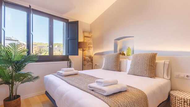Een slaapkamer met een groot bed, een potplant en uitzicht naar buiten.