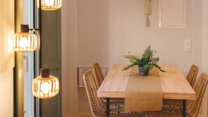 Een eetgedeelte met een houten tafel, rieten stoelen, een kamerplant varens en hanglampen.