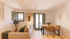 Een moderne woonkamer met een bank, een eettafel met stoelen, een potplant en een klein pouf.