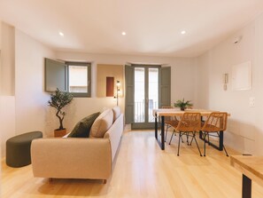 A modern living room with a sofa, a dining table with chairs, a potted plant, and a small ottoman. - Bravissimo Calderers La Daina, next to the Onyar (Girona)