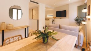 Een moderne woonkamer met een eethoek, een bank, een aan de muur bevestigde televisie en een plant op de tafel.