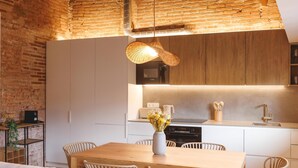 Eine moderne Küche mit weißen Schränken, einem Holztisch, Korbstühlen und einer Pendelleuchte.