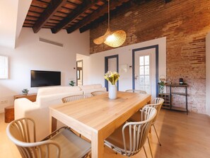 Un salon moderne avec une table à manger en bois, un canapé blanc et un téléviseur fixé au mur.