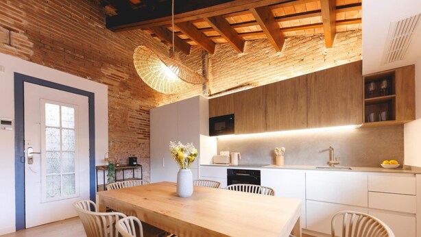 Eine moderne Küche mit Holztisch und -stühlen, einer Pendelleuchte und einer Backsteinwand.