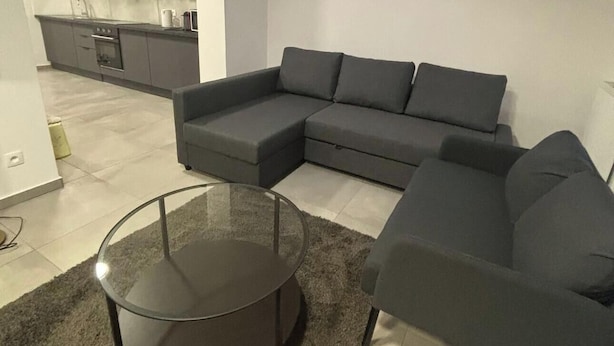Un salon moderne avec un canapé d’angle, une table basse en verre et une lucarne au plafond.