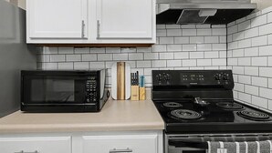 Una cocina con armarios blancos, un microondas negro, una estufa negra y un salpicadero de azulejos.