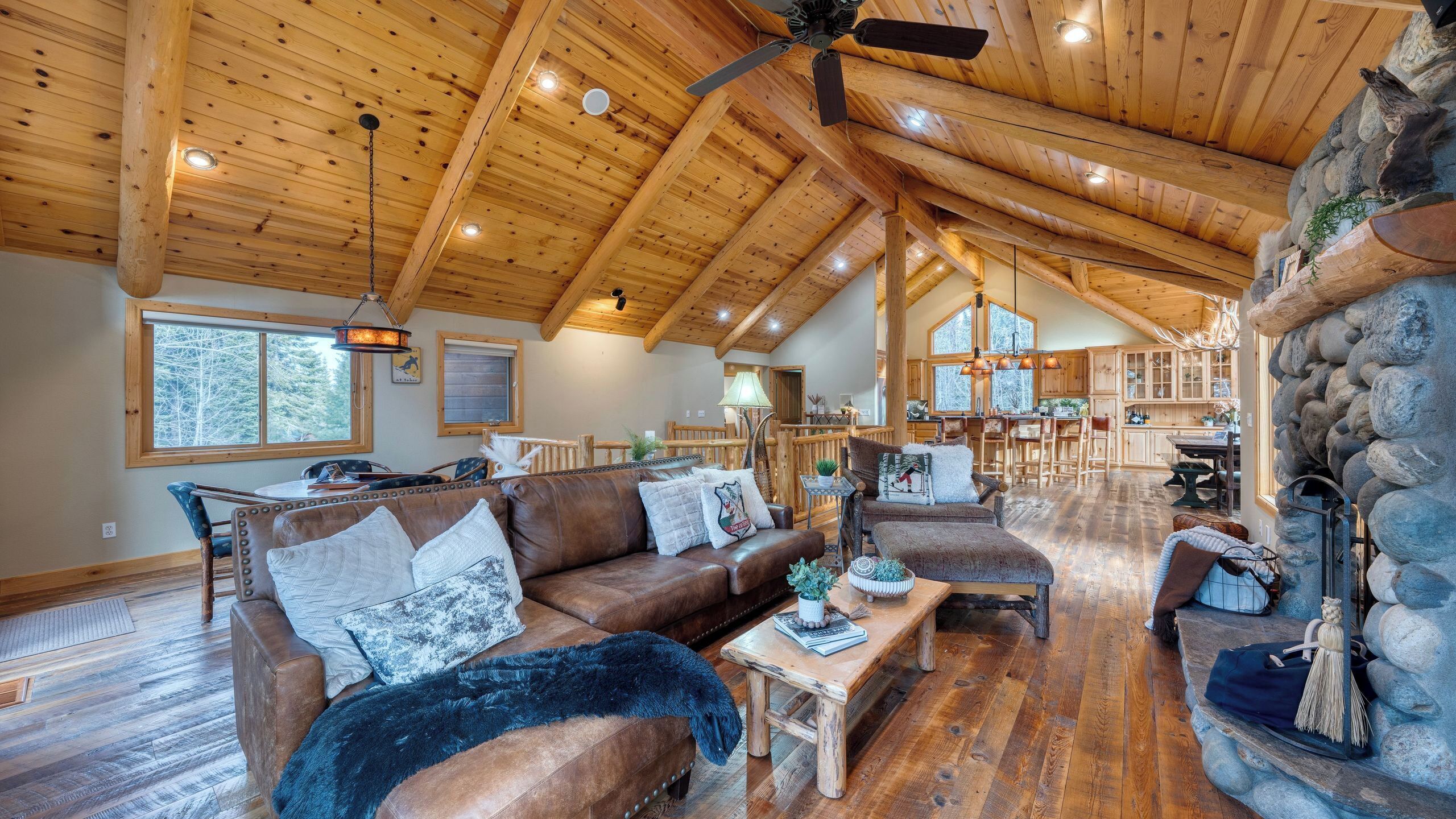 A spacious living area with a high ceiling, wooden beams, and a stone fireplace.