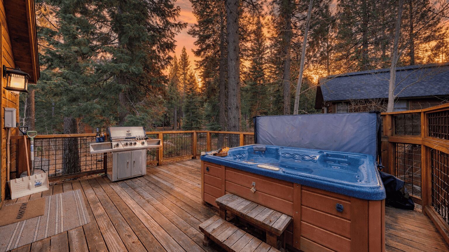A wooden deck with a hot tub, grill, and outdoor seating area surrounded by trees.