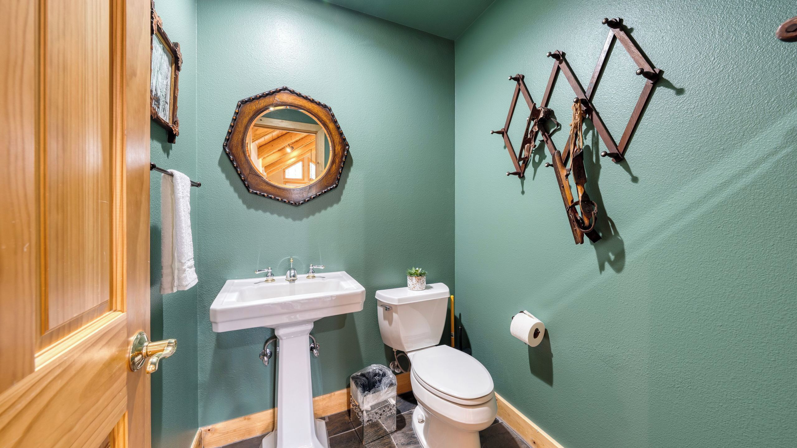 Une salle de bain avec un mur vert, une porte en bois, un lavabo blanc, des toilettes et un miroir.
