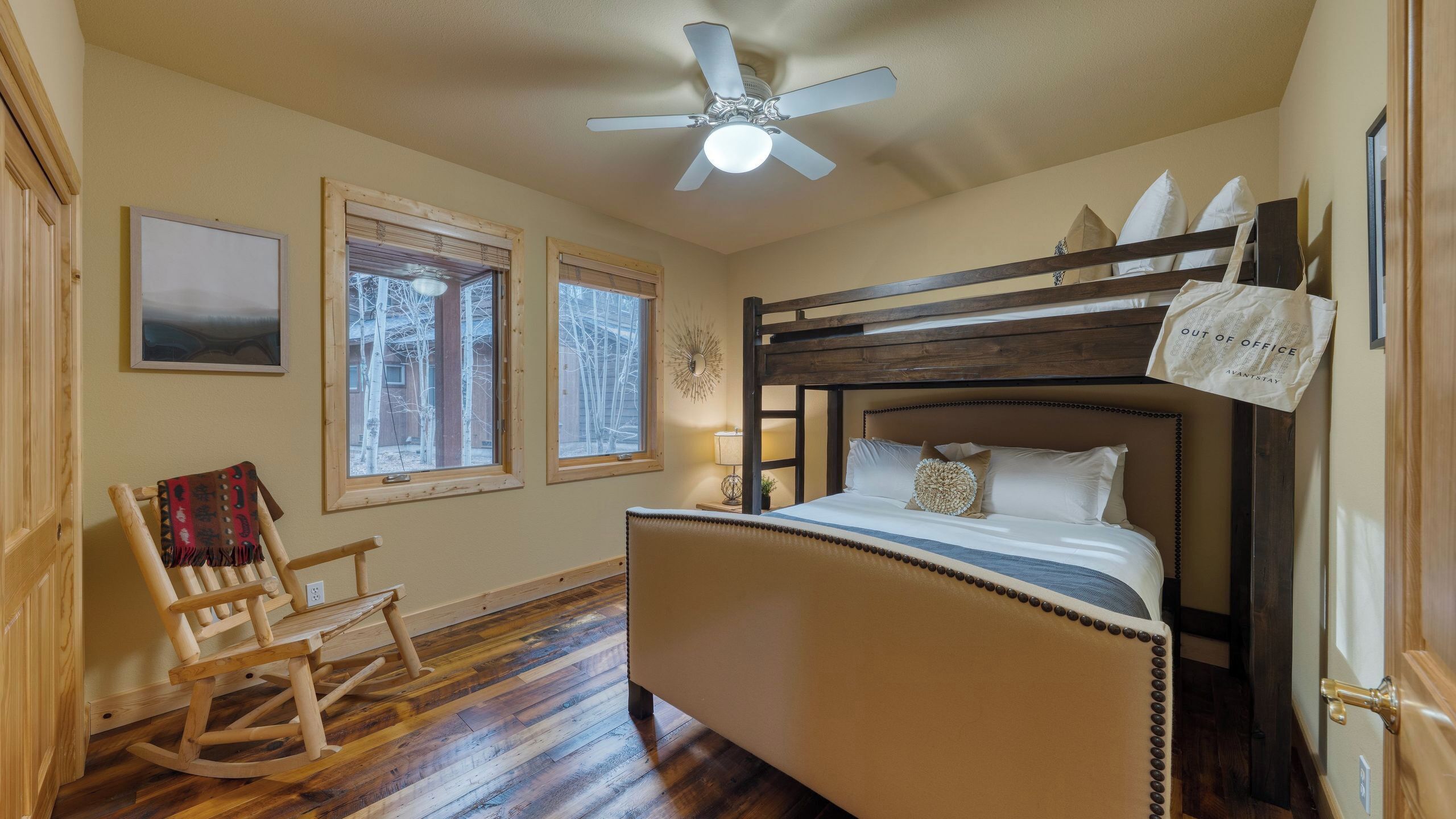 A bedroom with a bunk bed, a rocking chair, two windows, a ceiling fan, and a wall clock.