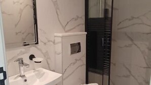Un baño moderno con salpicadero de mármol, un lavabo blanco, inodoro y cabina de ducha de cristal.