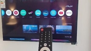 Una mano sostiene un control remoto frente a un televisor que muestra diferentes servicios de streaming.