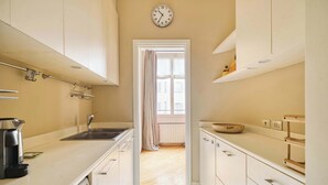 Eine schmale Küche mit weißen Schränken, einer Kaffeemaschine, einem Spülbecken und einer Uhr an der Wand.