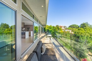 A modern balcony with a glass railing overlooking a lush garden and a residential area. - Beverly Hills Private Modern Escape (Beverly Hills)
