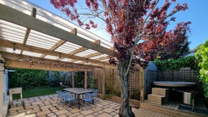 Un patio techado con una mesa y sillas de madera, rodeado por una terraza de madera y un jardín.