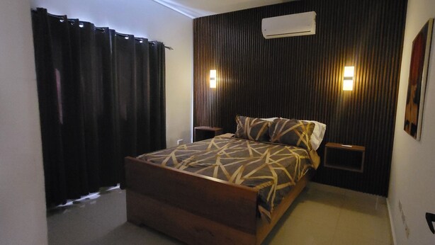 Ein Schlafzimmer mit Bett, Nachttisch, Wandklimaanlage und einem Fenster mit Vorhängen.