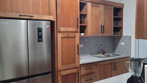 Eine Küche mit Holzschränken, einem Edelstahlkühlschrank, einer Granit Arbeitsplatte, einer Spüle und einem Mixer.