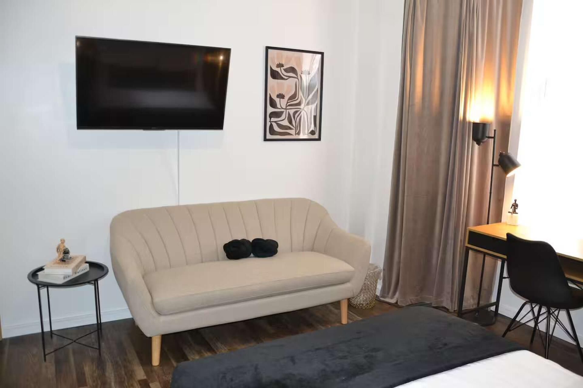 Habitación de hotel con sofá, televisión montada en la pared, escritorio con silla y lámpara.