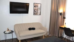 Une chambre d’hôtel équipée d’un canapé, d’un téléviseur fixé au mur, d’un bureau avec une chaise et d’une lampe.