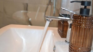 Une salle de bain avec un lavabo blanc, un robinet chromé et un flacon en verre marron.