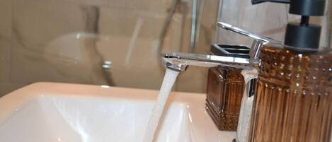 A bathroom with a white sink, a chrome faucet, and a brown glass bottle.