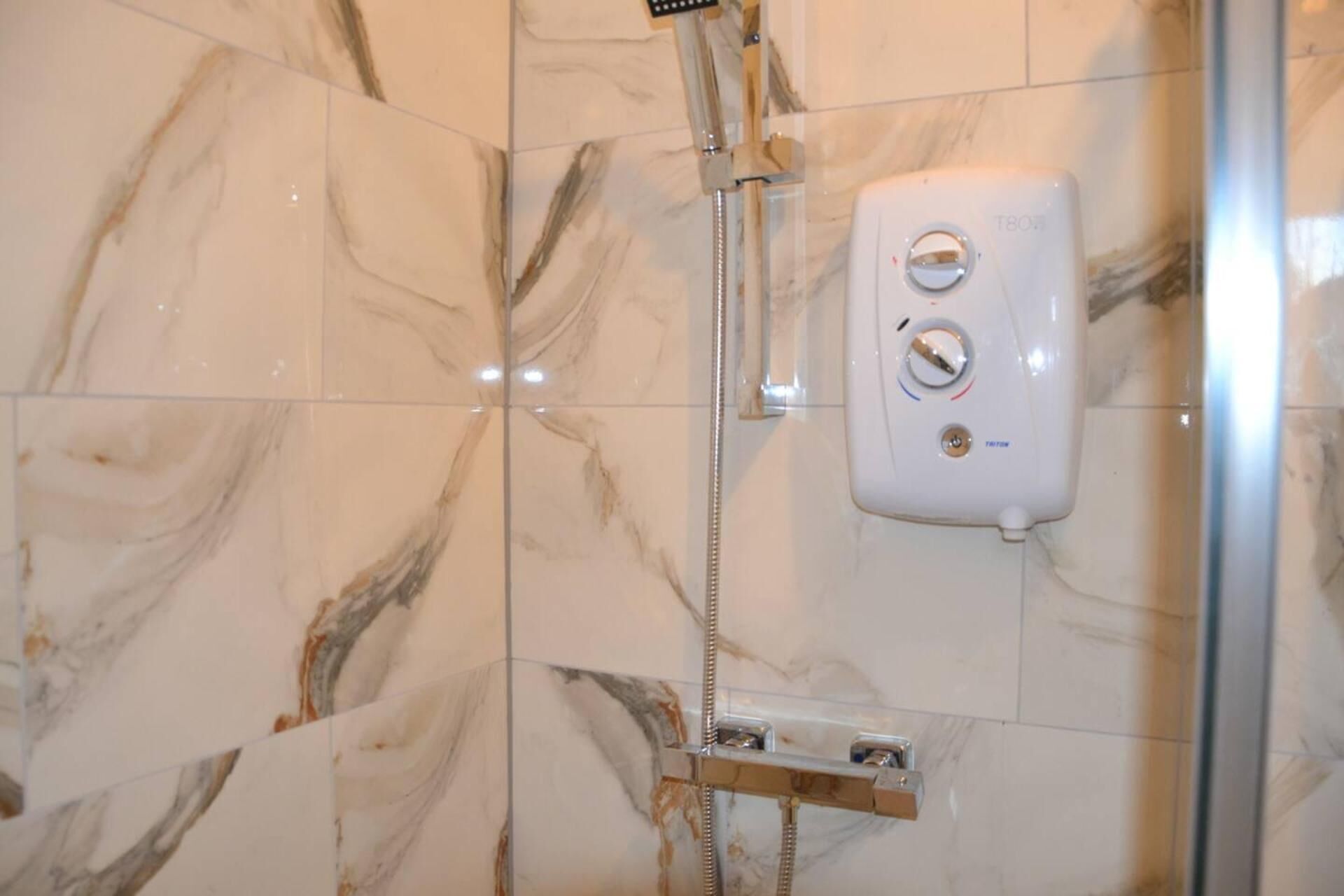 Ducha con cabezal de ducha de mano y panel de control en la pared.