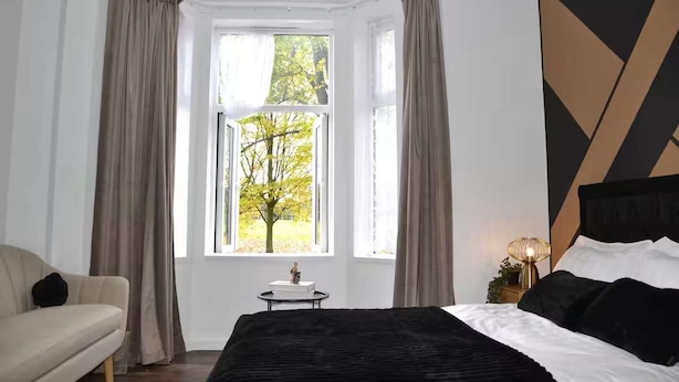 Une chambre à coucher avec un lit, une chaise, une table de chevet avec une lampe et une fenêtre avec des rideaux.