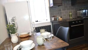 Un coin repas avec une table en bois dressée pour deux personnes, un pichet blanc et un vase de fleurs.
