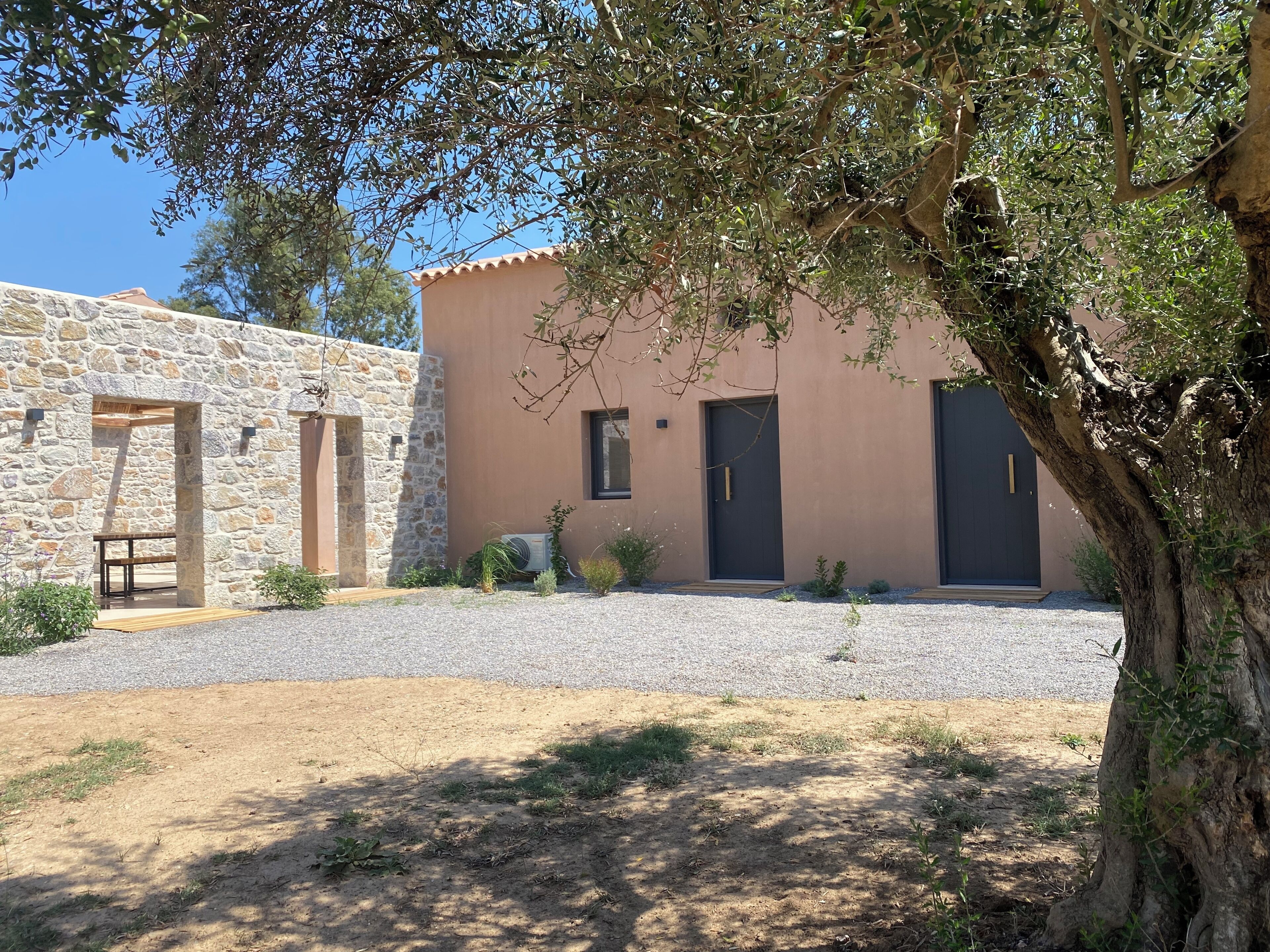 A stone building with a gravel driveway, a wooden bench, and a tree in the foreground.