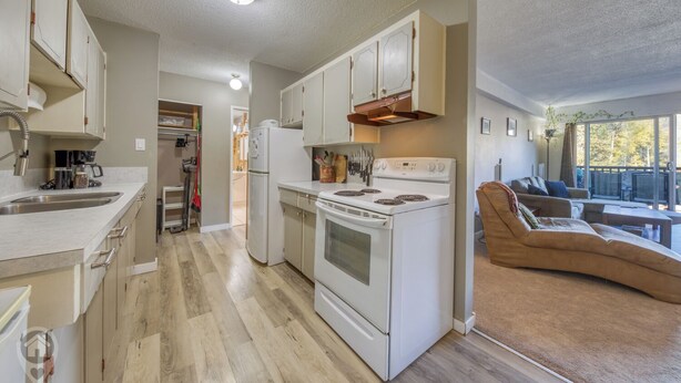 A modern kitchen with white appliances, a dining area with a brown sofa, and a large window offering a view. - Panoramic Mountain Views, Sauna, Pet Paradise (Fernie)