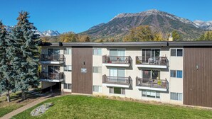 A multi-story apartment building with balconies, a sign indicating a powder ski resort nearby, and a mountain backdrop. - Panoramic Mountain Views, Sauna, Pet Paradise (Fernie)