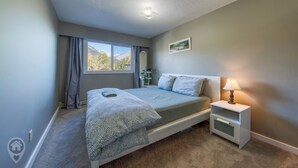 A bedroom with a bed, bedside table, lamp, and a window with curtains. - Panoramic Mountain Views, Sauna, Pet Paradise (Fernie)