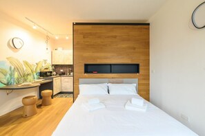 Ein modernes Hotelzimmer mit einem Holzkopfteil, einer kleinen Küchenzeile und einem großen Bett mit ordentlich gefalteten weißen Handtüchern.