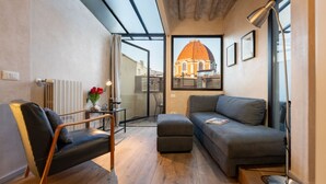 A modern living room with a sofa, ottoman, and a chair, a radiator, a table with a vase, and a framed picture of a building. - San Lorenzo Terrace Apartment (Florence)