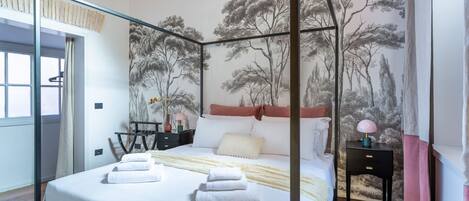 A bedroom with a four-poster bed, a nightstand, a lamp, and a mural of trees on the wall.