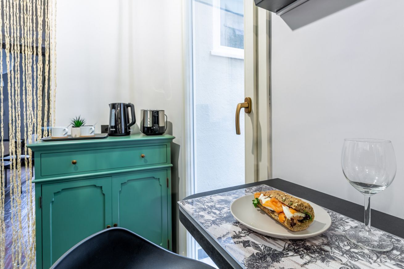 A small kitchenette with a teal cabinet, a coffee maker, and a plate with a sandwich.